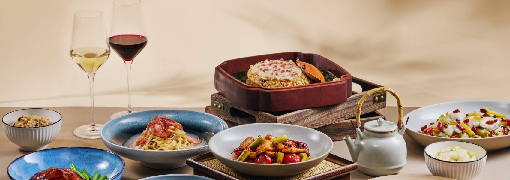 An assortment of dishes from Cathay Pacific's Chinese Classics series. The dishes are arranged on a table alongside a teapot and two glasses of wine. 